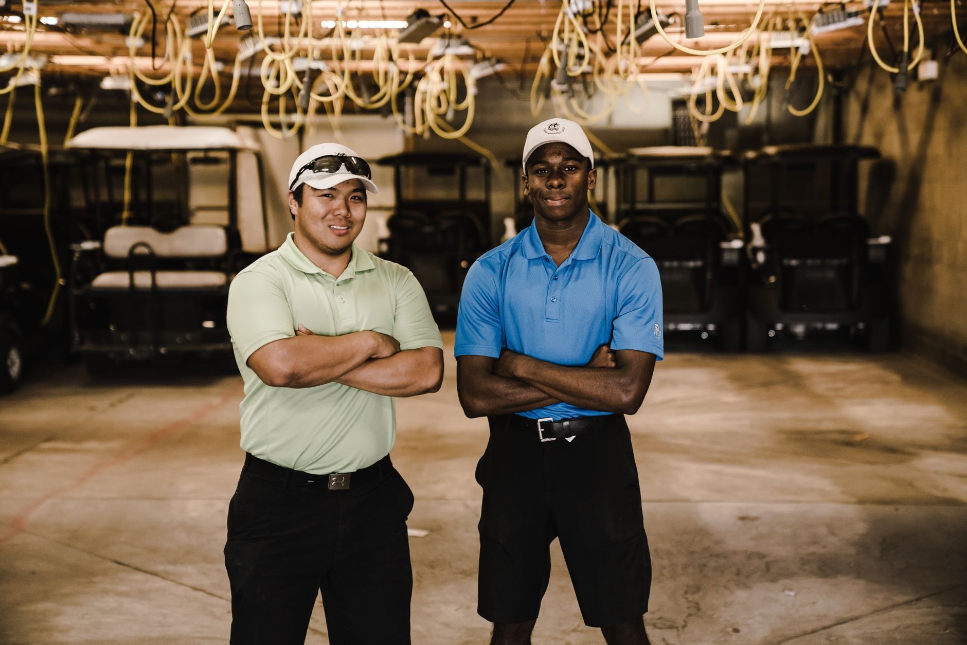Two golf cart service technicians standing in front of rows of carts and charging cables